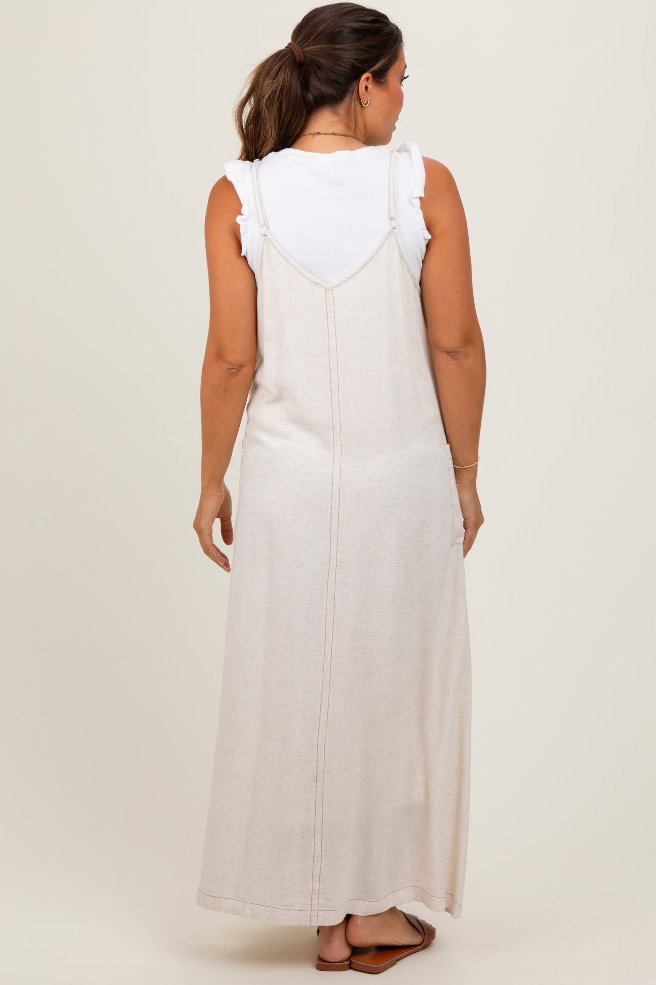 woman wearing a maternity cream maxi dress over a white ruffled top, viewed from the back