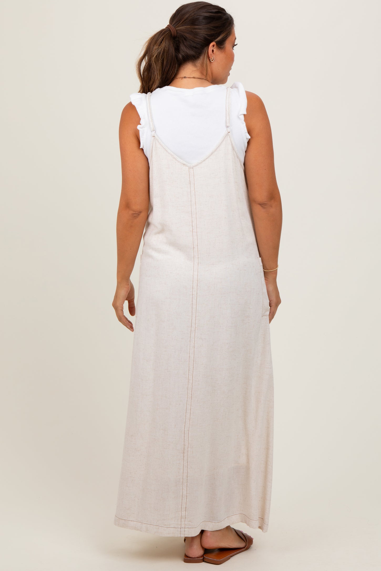 woman wearing a maternity cream maxi dress over a white ruffled top, viewed from the back
