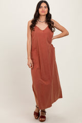 woman wearing a rust-colored sleeveless maxi dress with a v-neck and front pockets