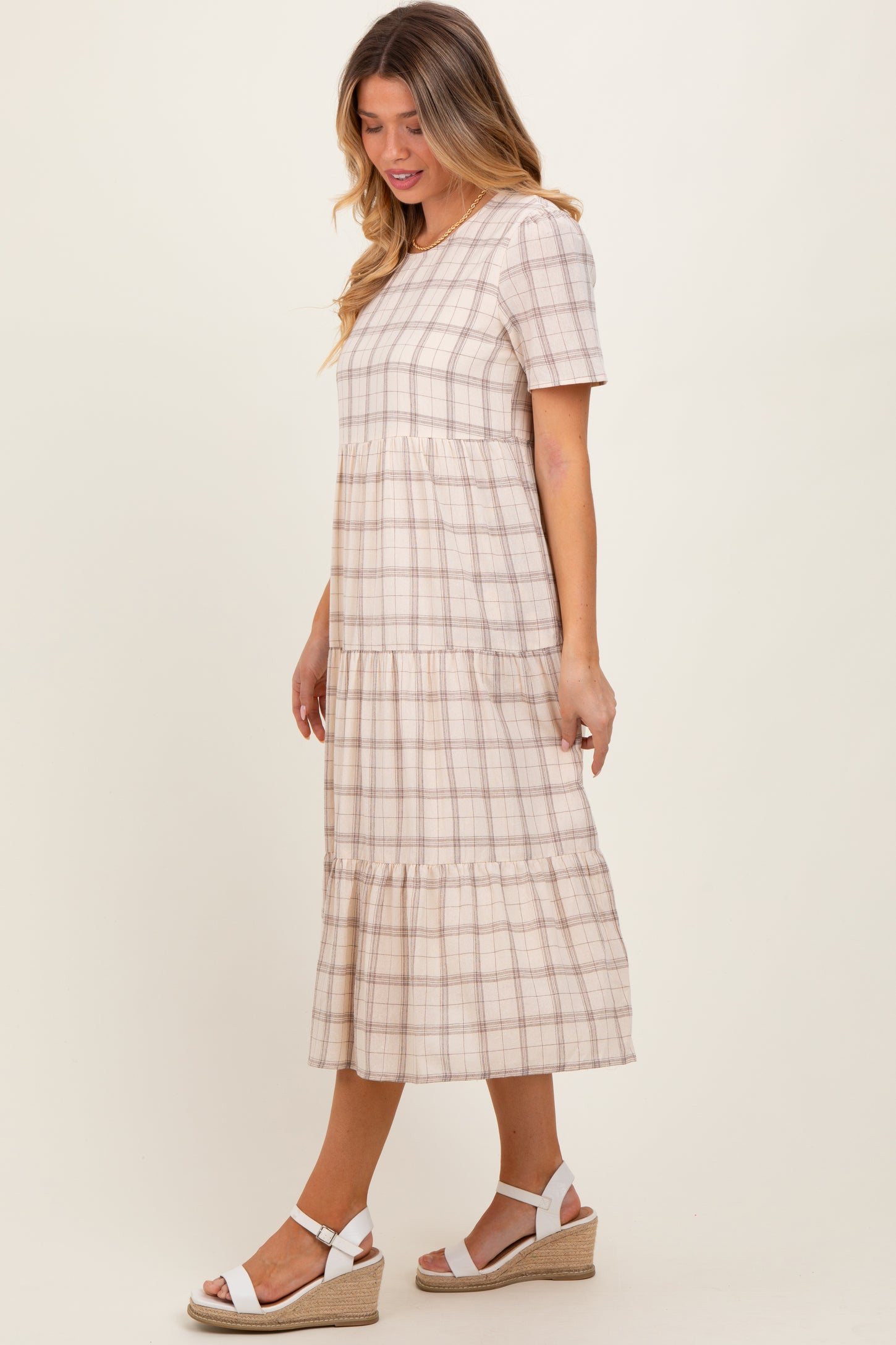 woman wearing a beige plaid tiered midi dress with short sleeves and a flared skirt, paired with white wedge sandals