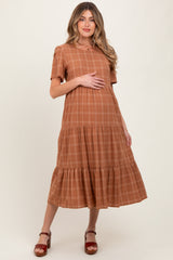 woman wearing a brown plaid short sleeve maternity dress with tiered skirt and holding her baby bump