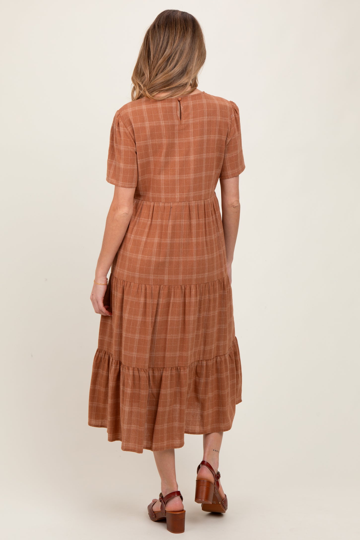 woman wearing a brown plaid maternity dress with short sleeves and a tiered skirt, showing her baby bump from the back