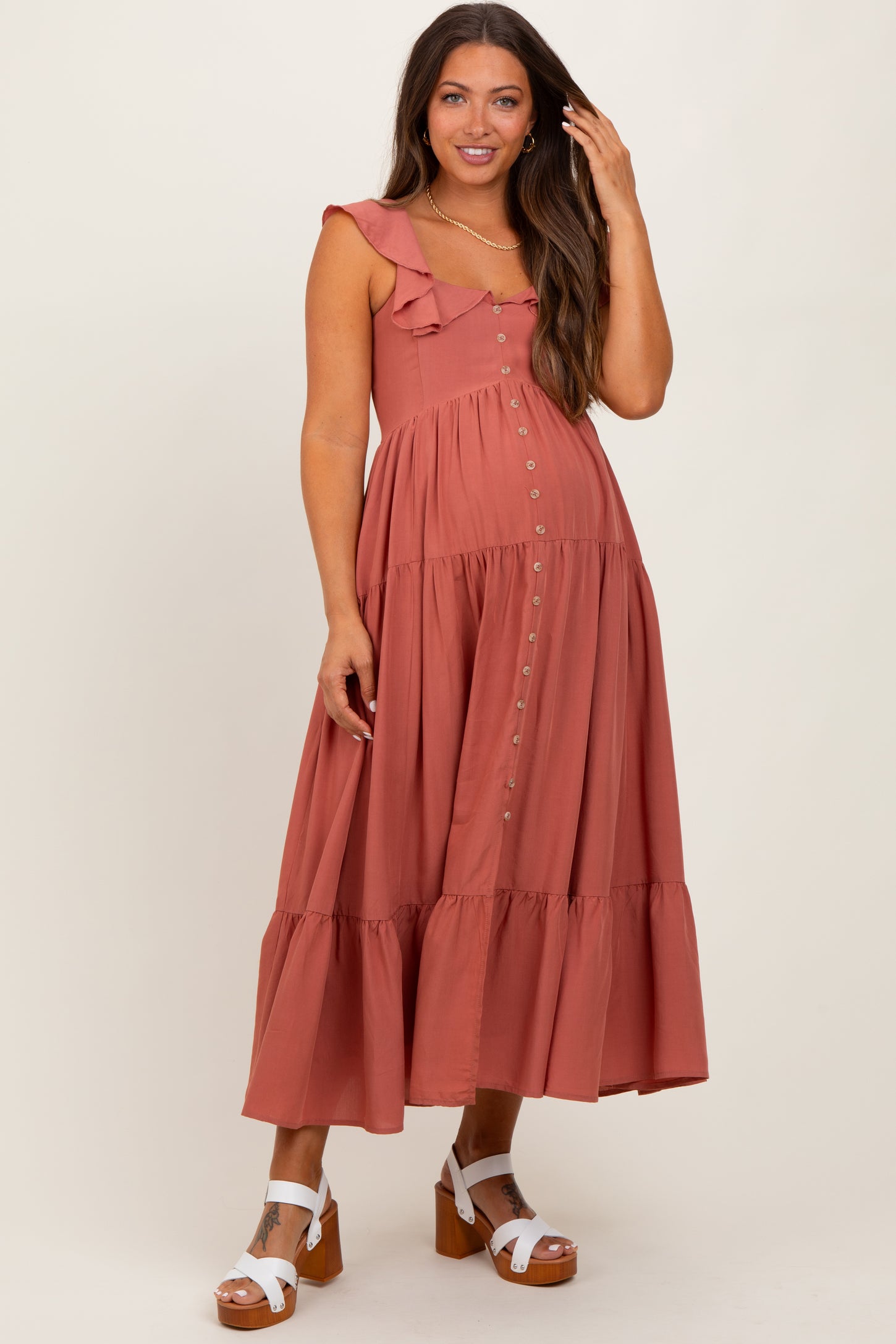 woman wearing a rust colored maternity dress with ruffle straps and a tiered skirt, standing and smiling