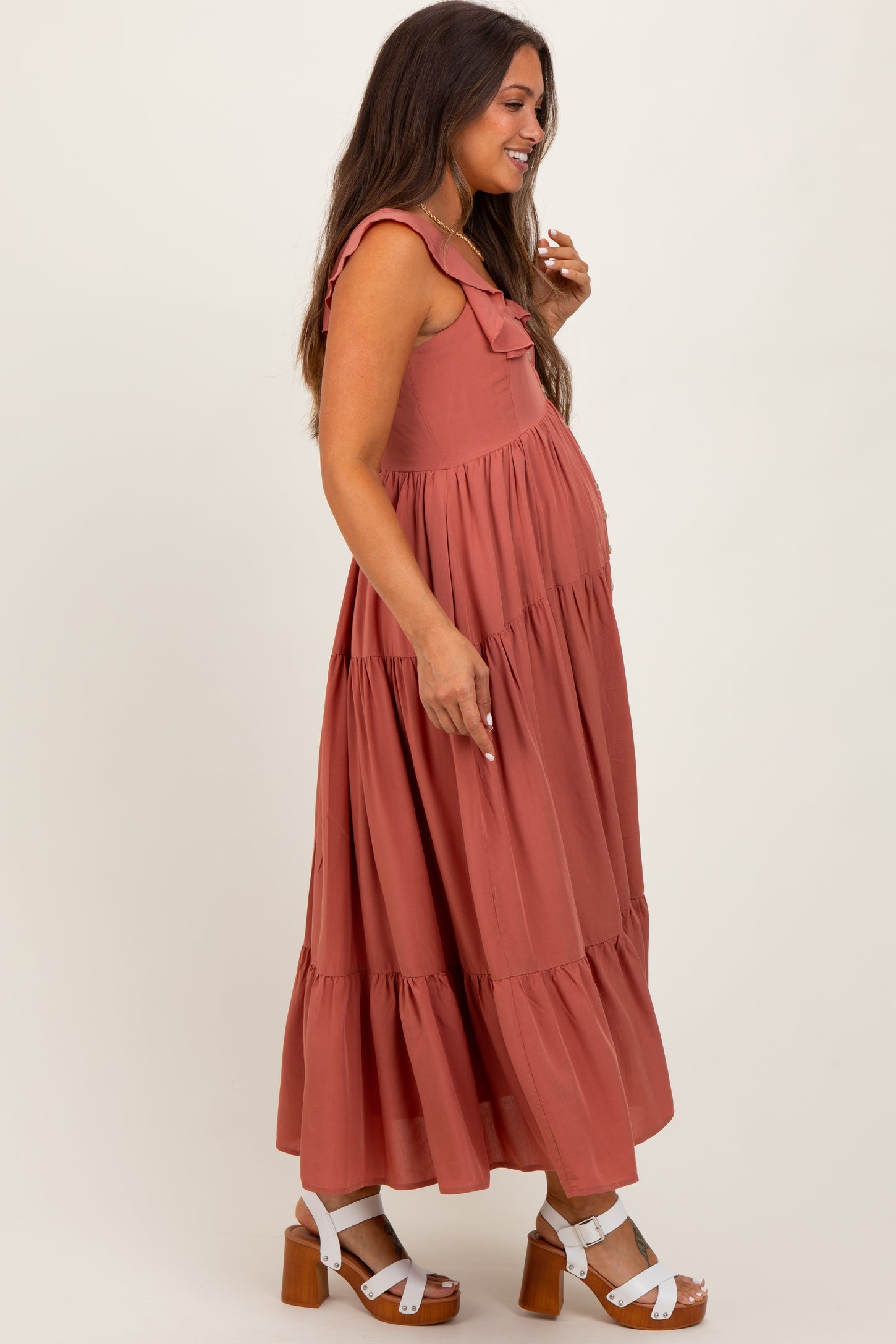 woman wearing a rust-colored maternity maxi dress with ruffle details and a visible baby bump