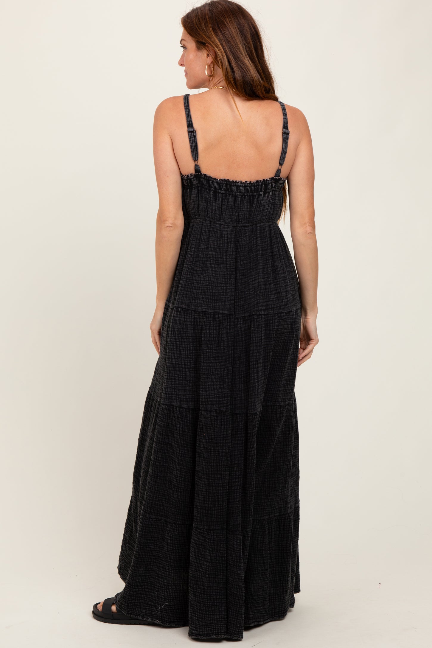 woman wearing a black maxi dress with adjustable straps and tiered detailing, shown from the back