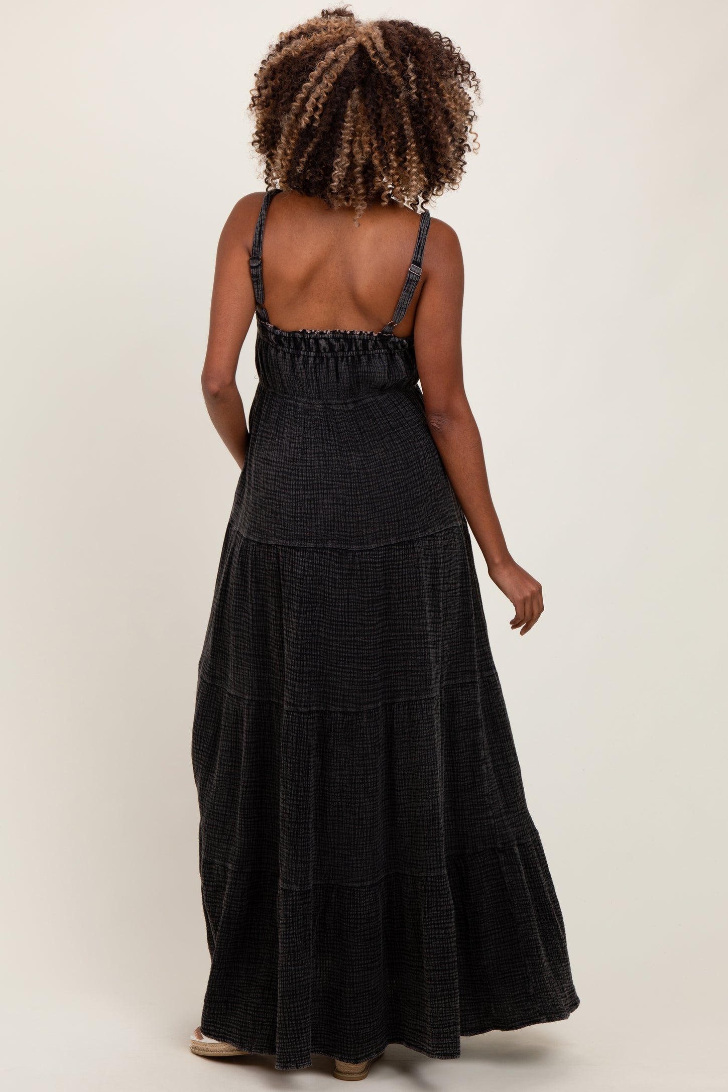 woman wearing a black tiered maxi maternity dress with adjustable straps and smocked back detail