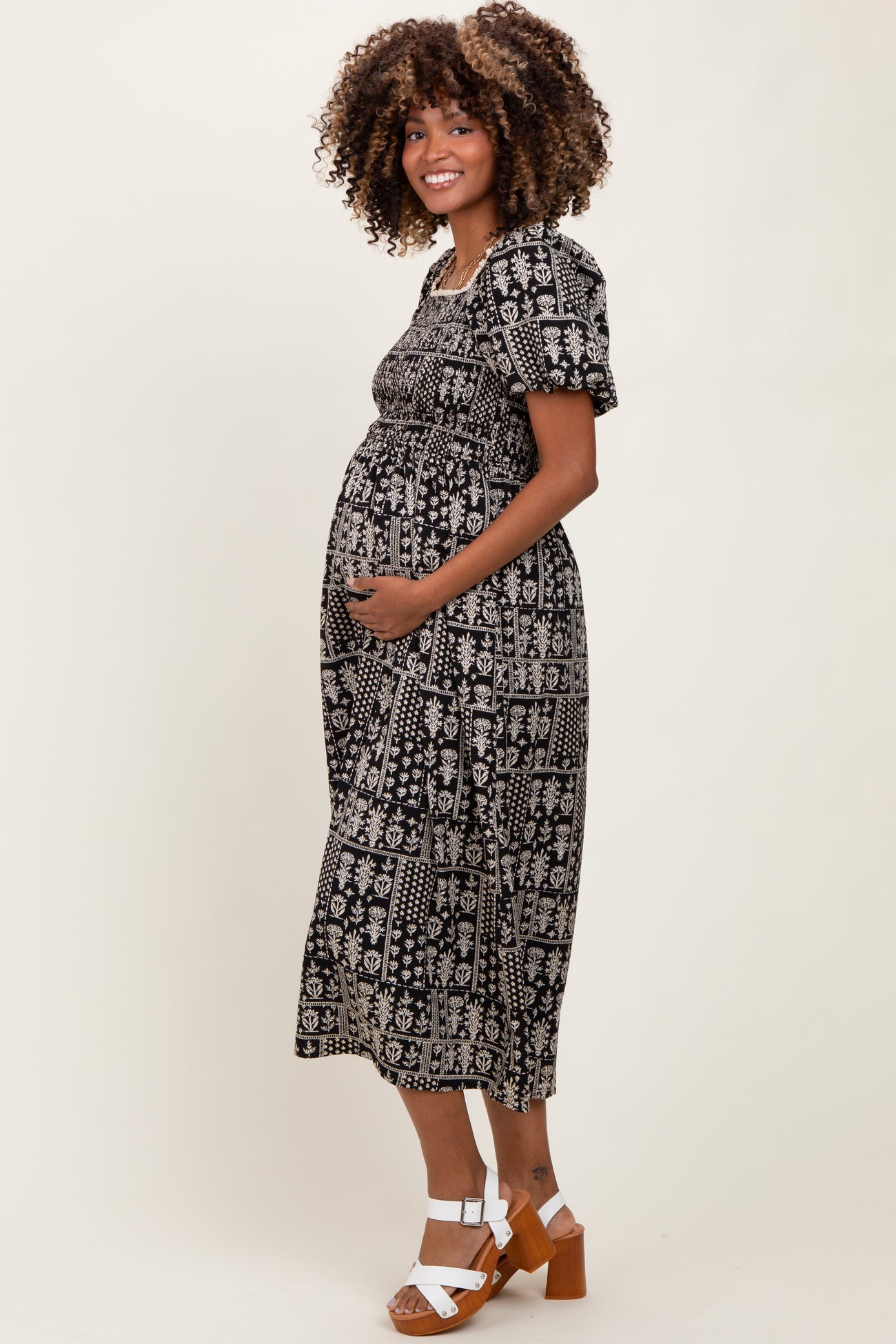 woman wearing a black and white patterned maternity dress and cradling her baby bump