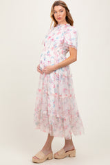 woman wearing a floral maternity dress with ruffled tiers and short sleeves, holding her baby bump