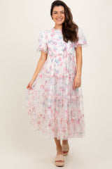 woman wearing a floral tiered maxi dress with short sleeves and a cinched waist, standing in front of a neutral background