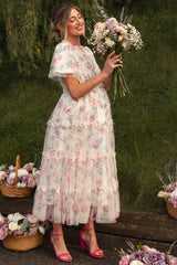 woman wearing a white floral maternity dress with ruffles and holding a bouquet, showing her baby bump