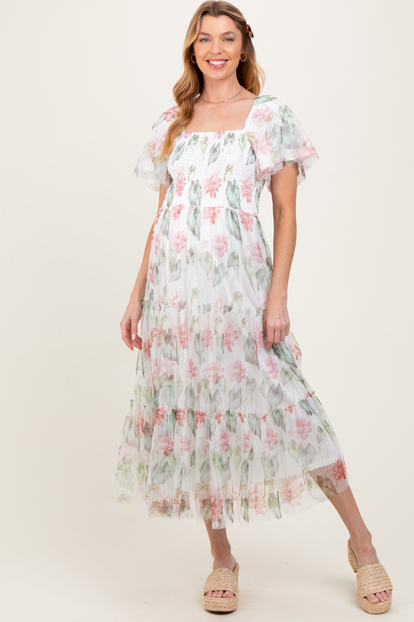 woman wearing a floral printed maternity maxi dress with puff sleeves and a tiered skirt, smiling at the camera