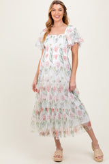 woman wearing a floral printed maternity maxi dress with puff sleeves and a tiered skirt, smiling at the camera