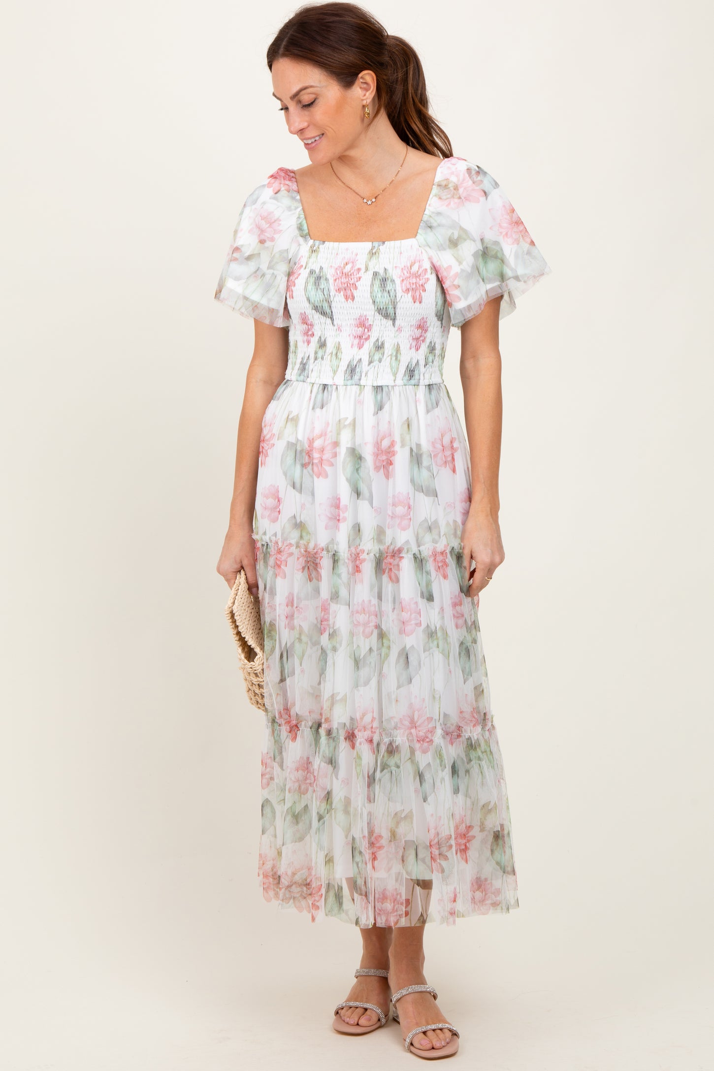 woman wearing a white floral maxi dress with puff sleeves and a square neckline, holding a clutch purse