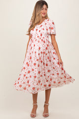 woman wearing a floral smocked maternity dress with short sleeves and a flowing skirt, highlighting her baby bump