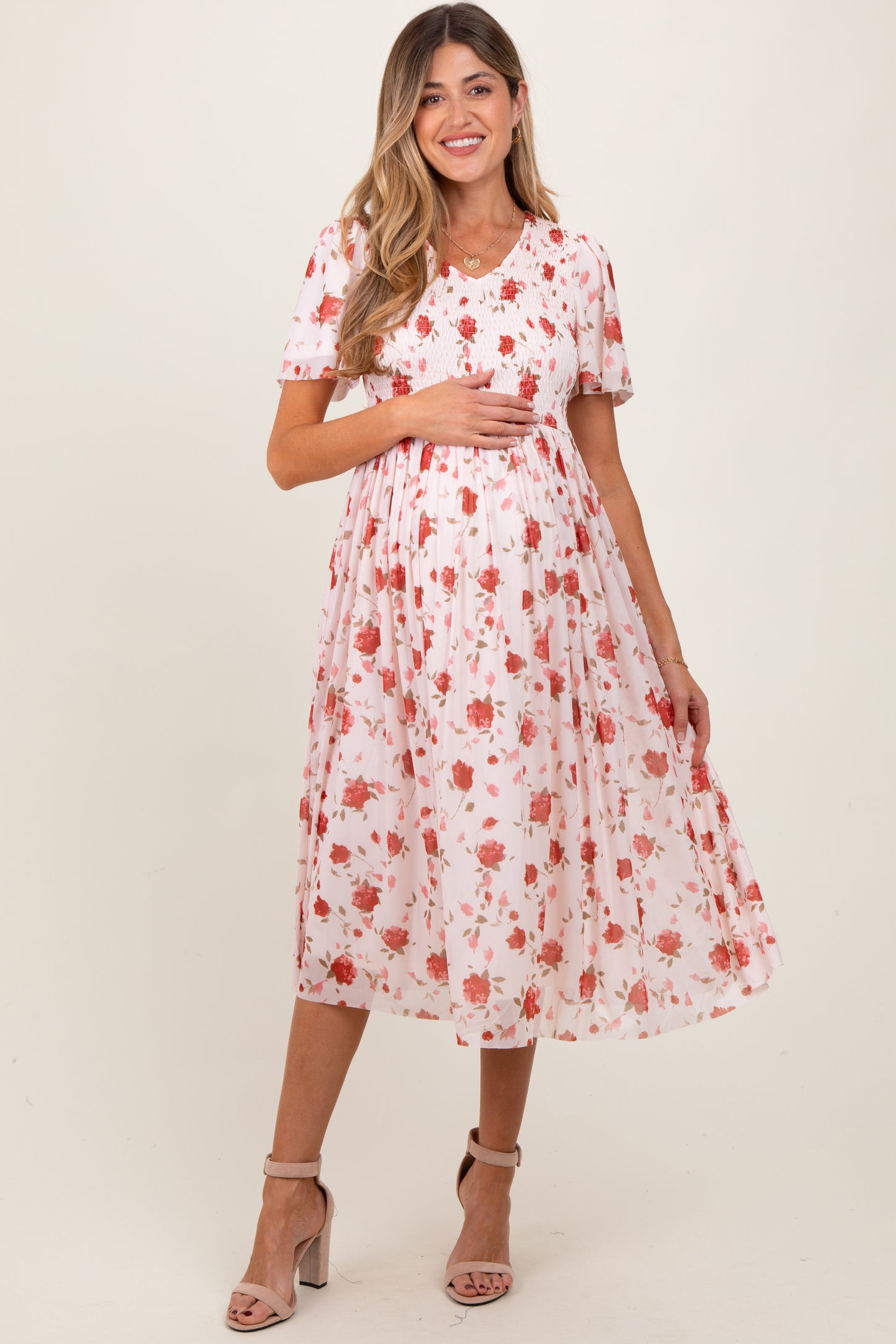 woman wearing a pink floral maternity dress with short sleeves and a smocked bodice, holding her baby bump