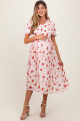 woman wearing a pink floral maternity dress with short sleeves and a smocked bodice, holding her baby bump