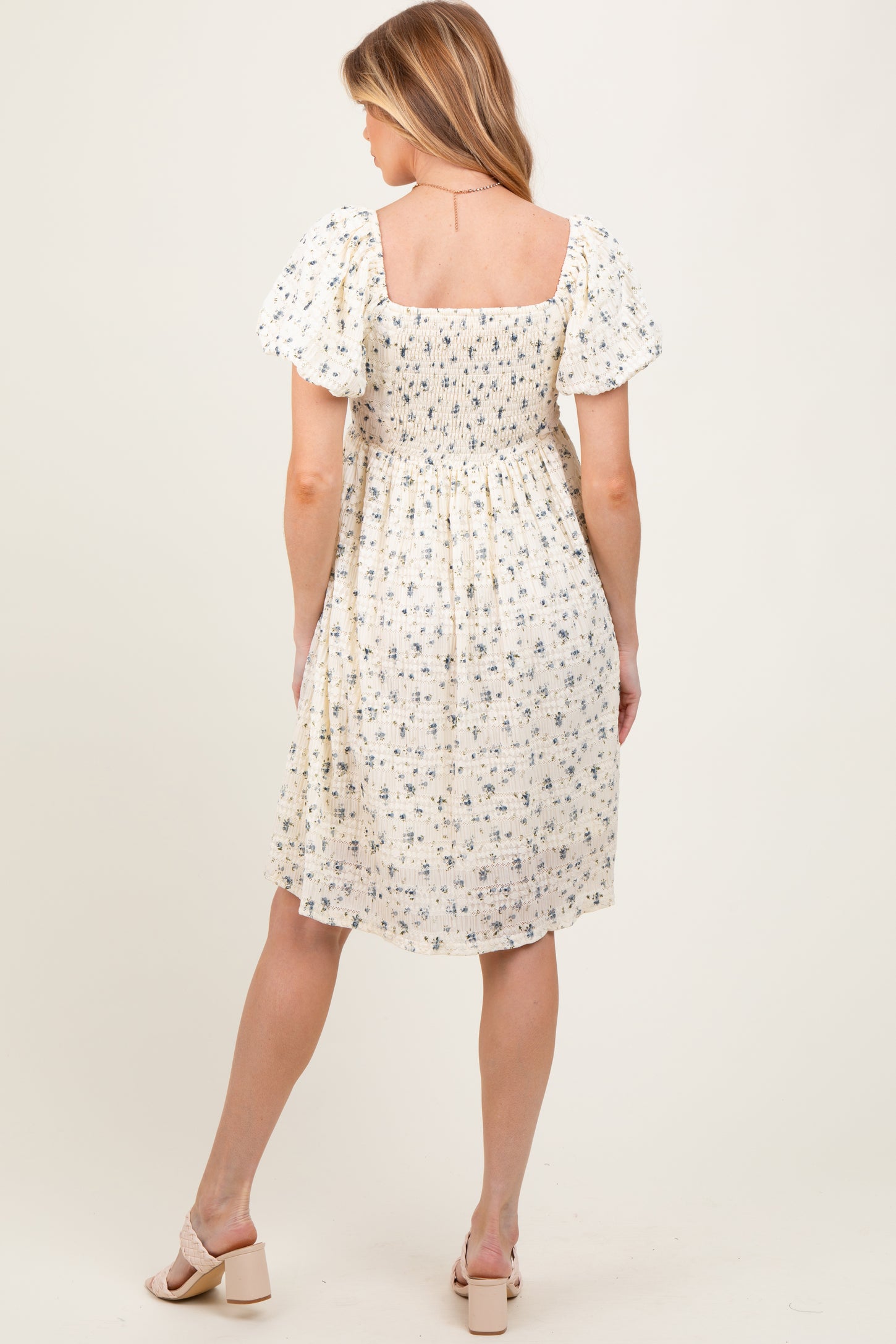 woman wearing a short, floral maternity dress with puff sleeves and a square neckline, showing her baby bump from the back