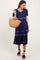 woman wearing a navy blue short sleeve dress with floral embroidery and holding a straw bag