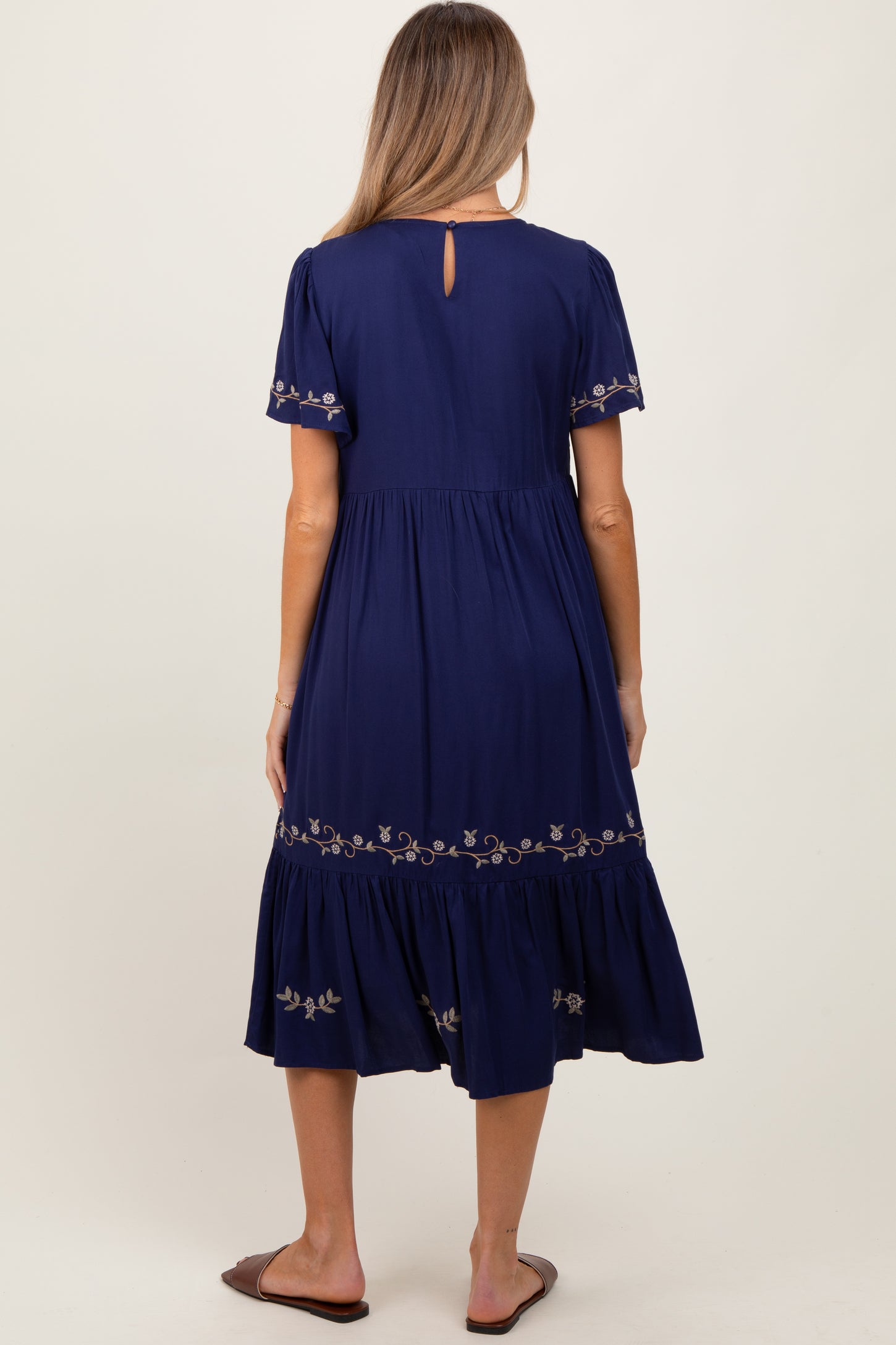 woman wearing a navy blue maternity dress with floral embroidery and a flowy skirt, showing a baby bump from the back
