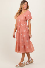 woman wearing a coral puff sleeve midi dress with floral embroidery and tiered skirt, standing on a light background