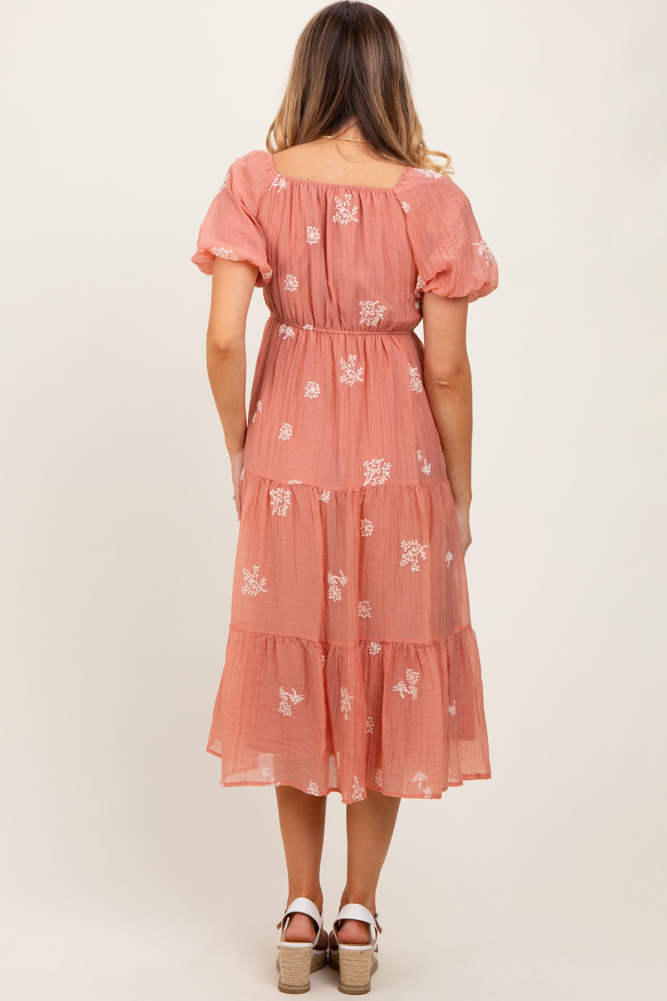 woman wearing a pink floral embroidered maxi dress with puff sleeves and a tiered skirt