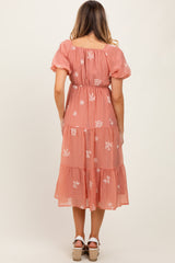 woman wearing a pink floral embroidered maxi dress with puff sleeves and a tiered skirt