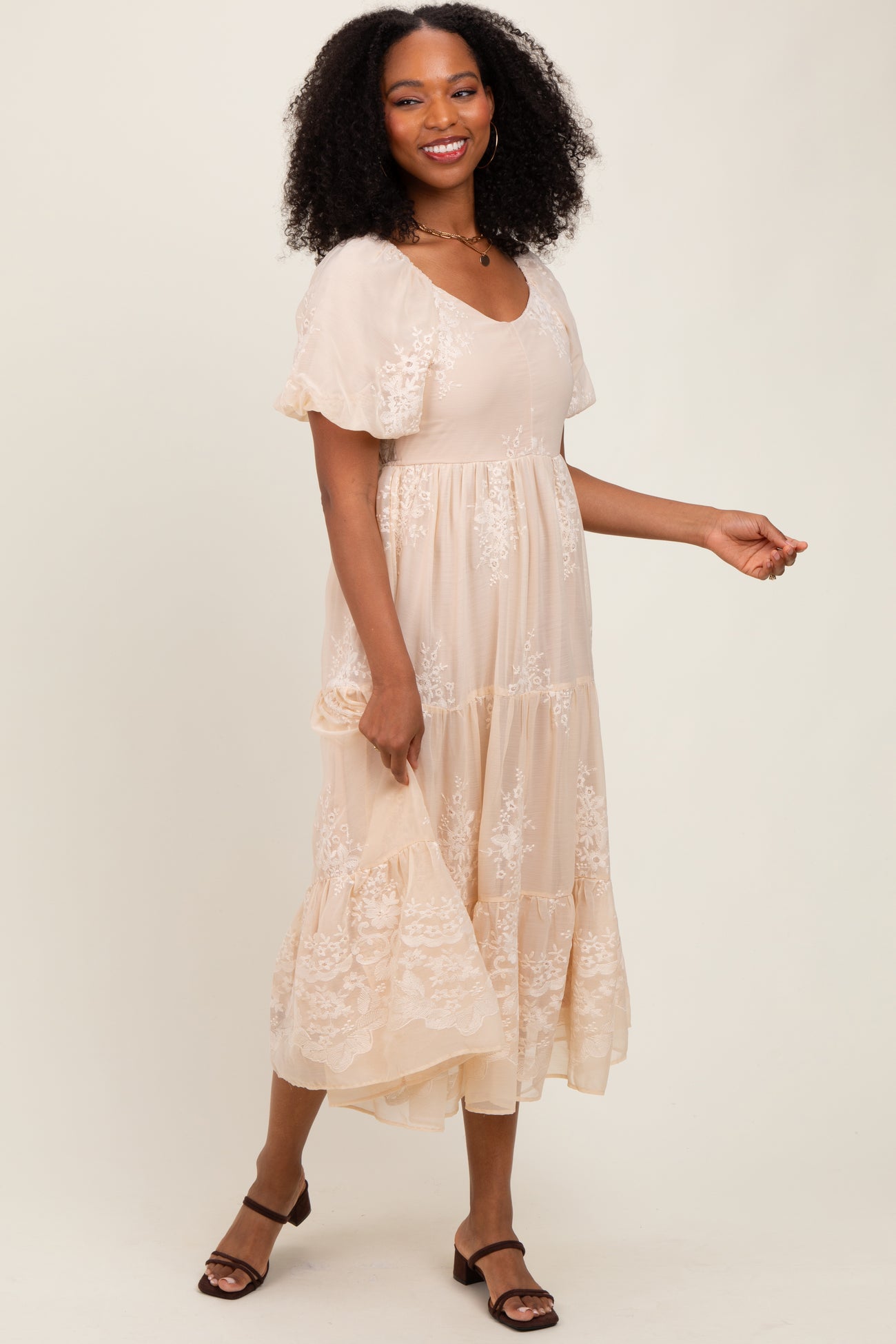 woman wearing a blush pink maxi dress with floral embroidery and flutter sleeves, standing and smiling
