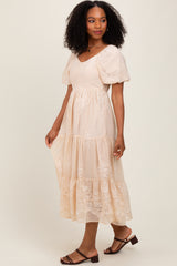 woman wearing a beige midi dress with puff sleeves and floral embroidery, standing in profile