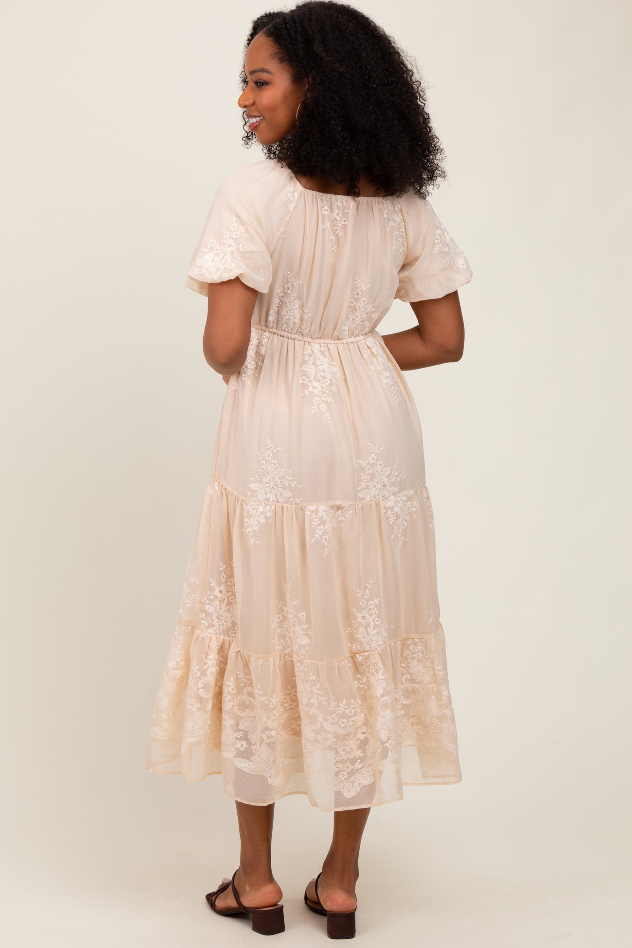 woman wearing a nude tiered maxi dress with floral embroidery details and short sleeves, viewed from the back