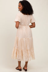 woman wearing a nude tiered maxi dress with floral embroidery details and short sleeves, viewed from the back