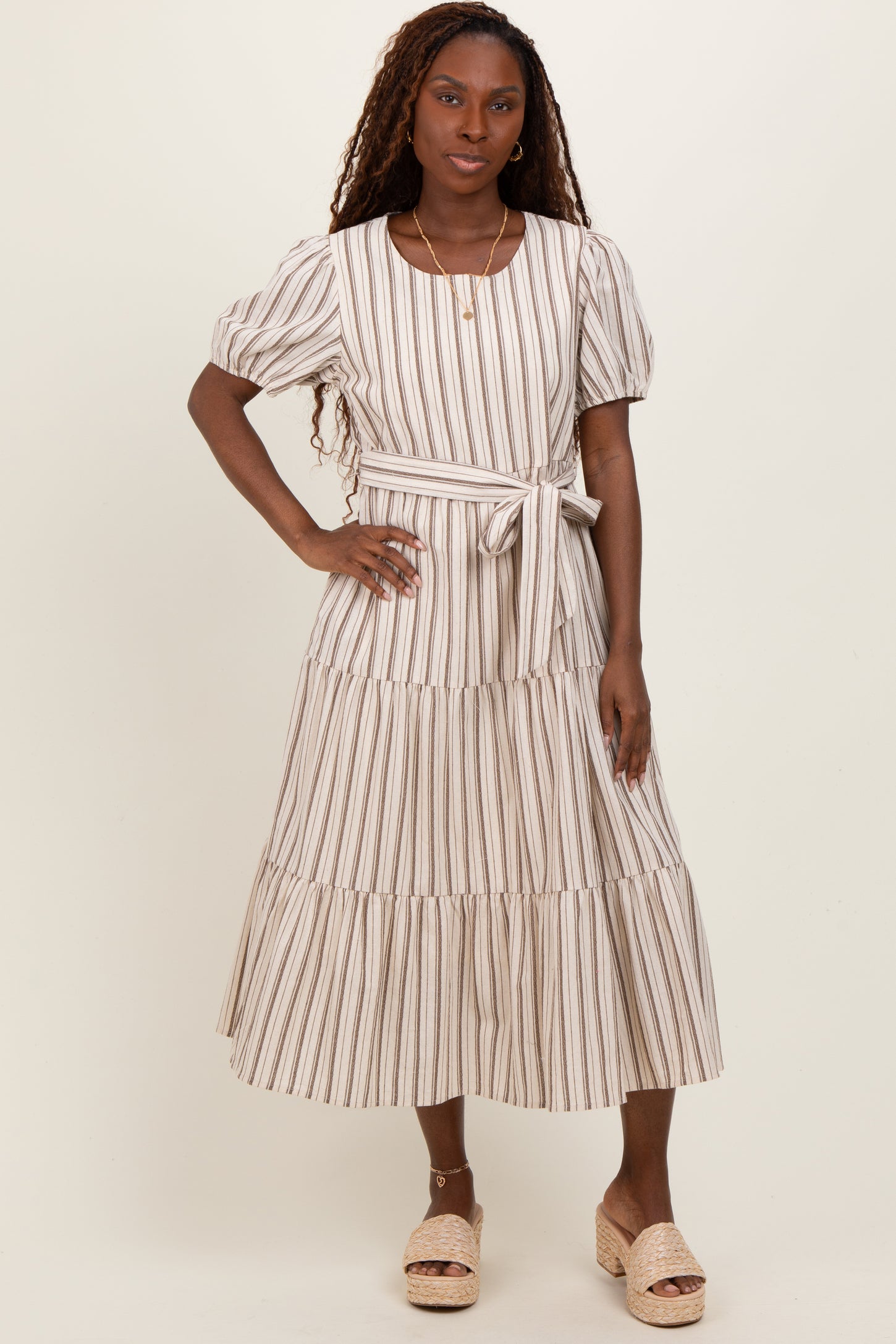 woman wearing a striped midi dress with puff sleeves and a tie belt, standing on a light background