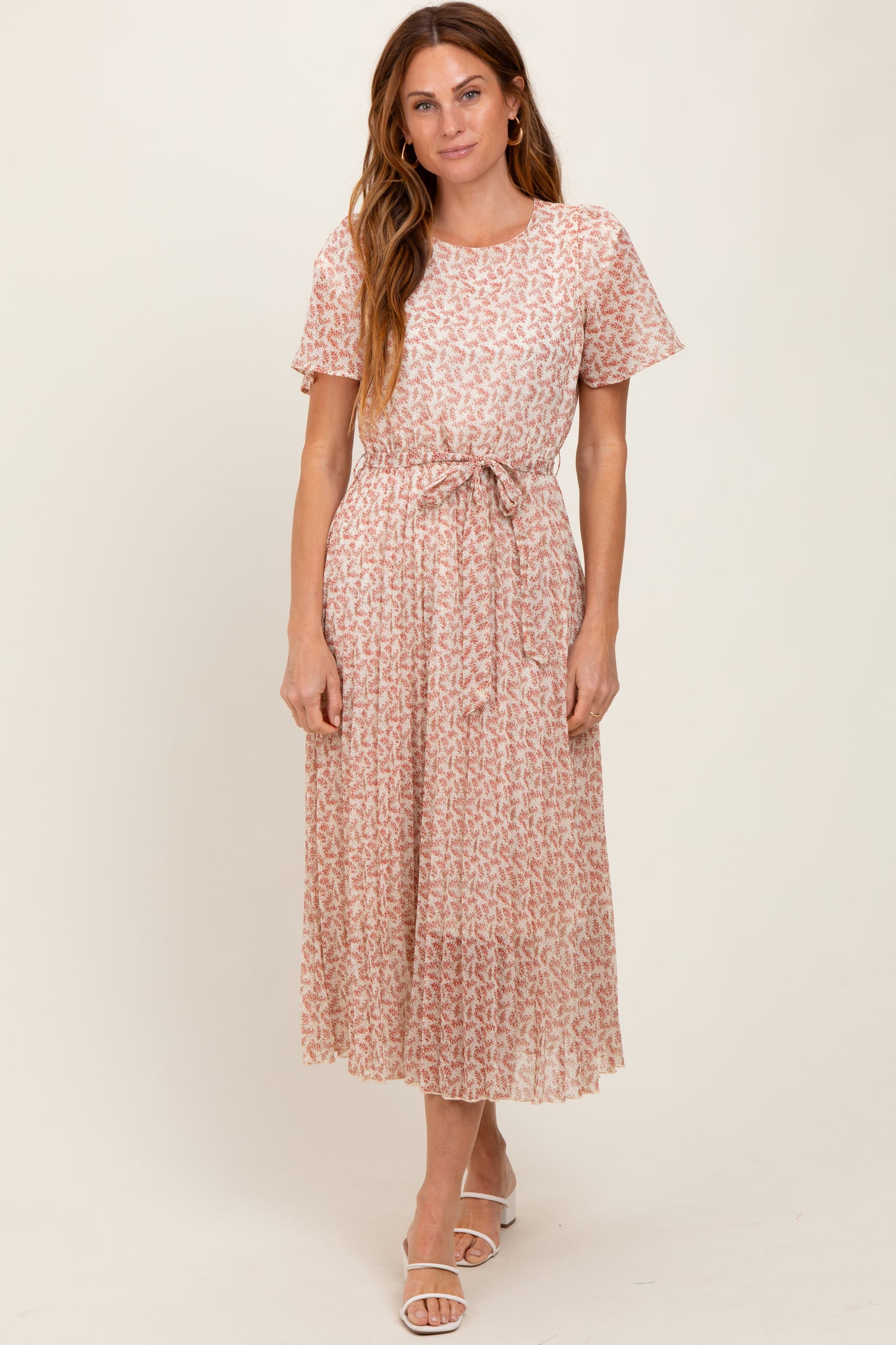 woman wearing a light pink floral midi dress with short sleeves and a tie belt at the waist