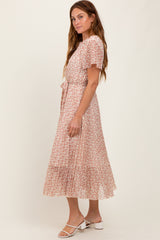 woman wearing a blush pink floral midi dress with short ruffled sleeves and a tie waist detail