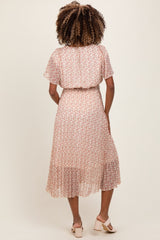 woman wearing a blush pink floral maternity dress with flutter sleeves and a tiered skirt, showing her baby bump from the back