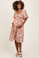 woman wearing a floral maternity dress with puff sleeves and a smocked bodice, cradling her baby bump