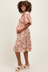 woman wearing a floral print maternity dress with puff sleeves and a baby bump visible, standing and smiling