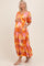 woman wearing a vibrant floral print maternity maxi dress with puff sleeves and pockets, holding her baby bump