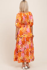 woman wearing a vibrant orange floral maternity maxi dress with puffed sleeves and a fitted bodice, seen from the back