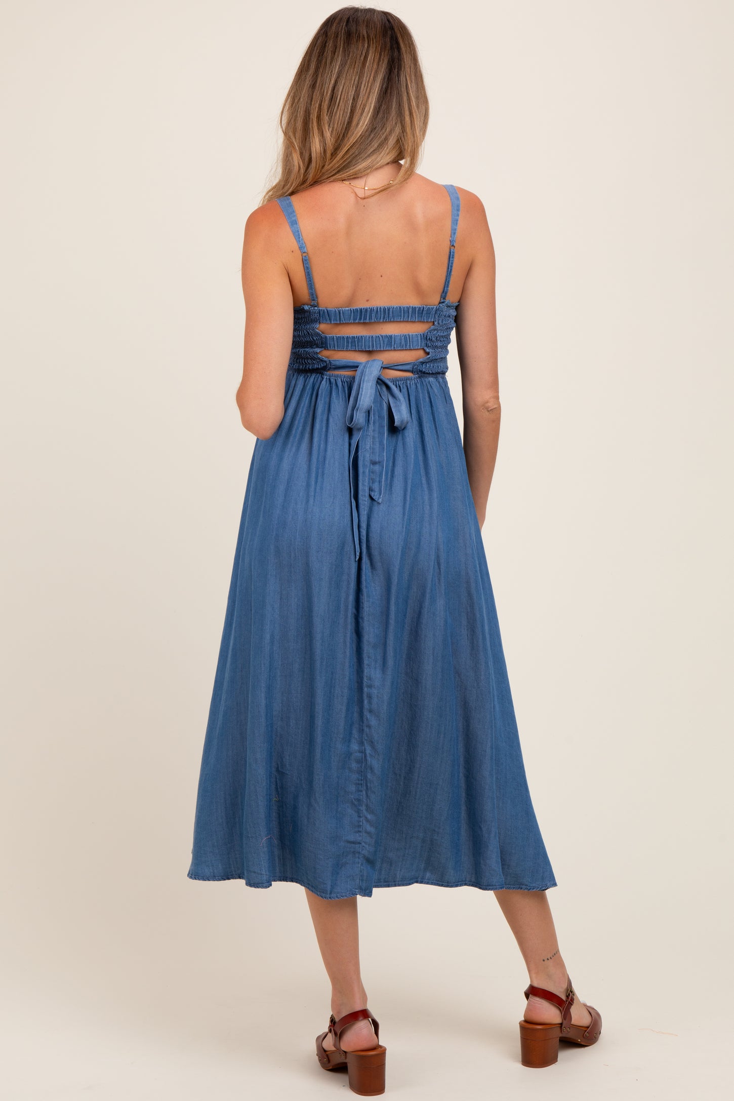 woman wearing a blue maternity dress with a smocked back and tie detail, showing a flowing midi length style