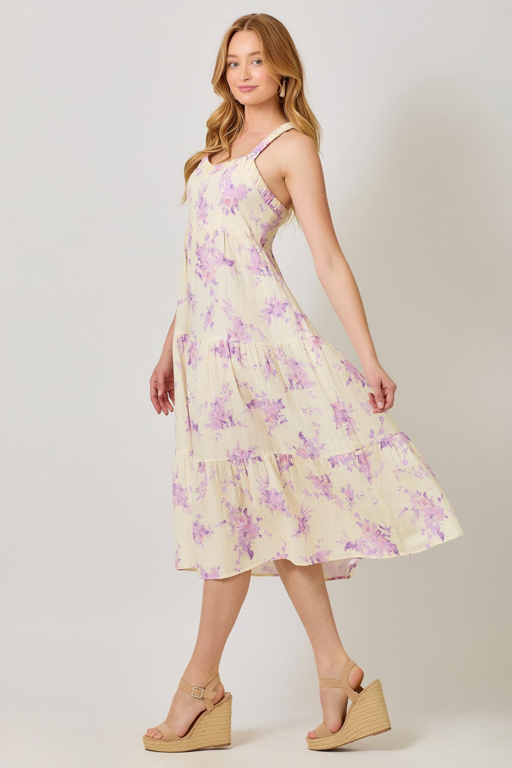 woman wearing a yellow floral midi dress with adjustable straps and a tiered skirt, paired with wedge sandals