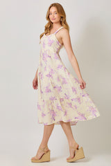 woman wearing a yellow floral midi dress with adjustable straps and a tiered skirt, paired with wedge sandals