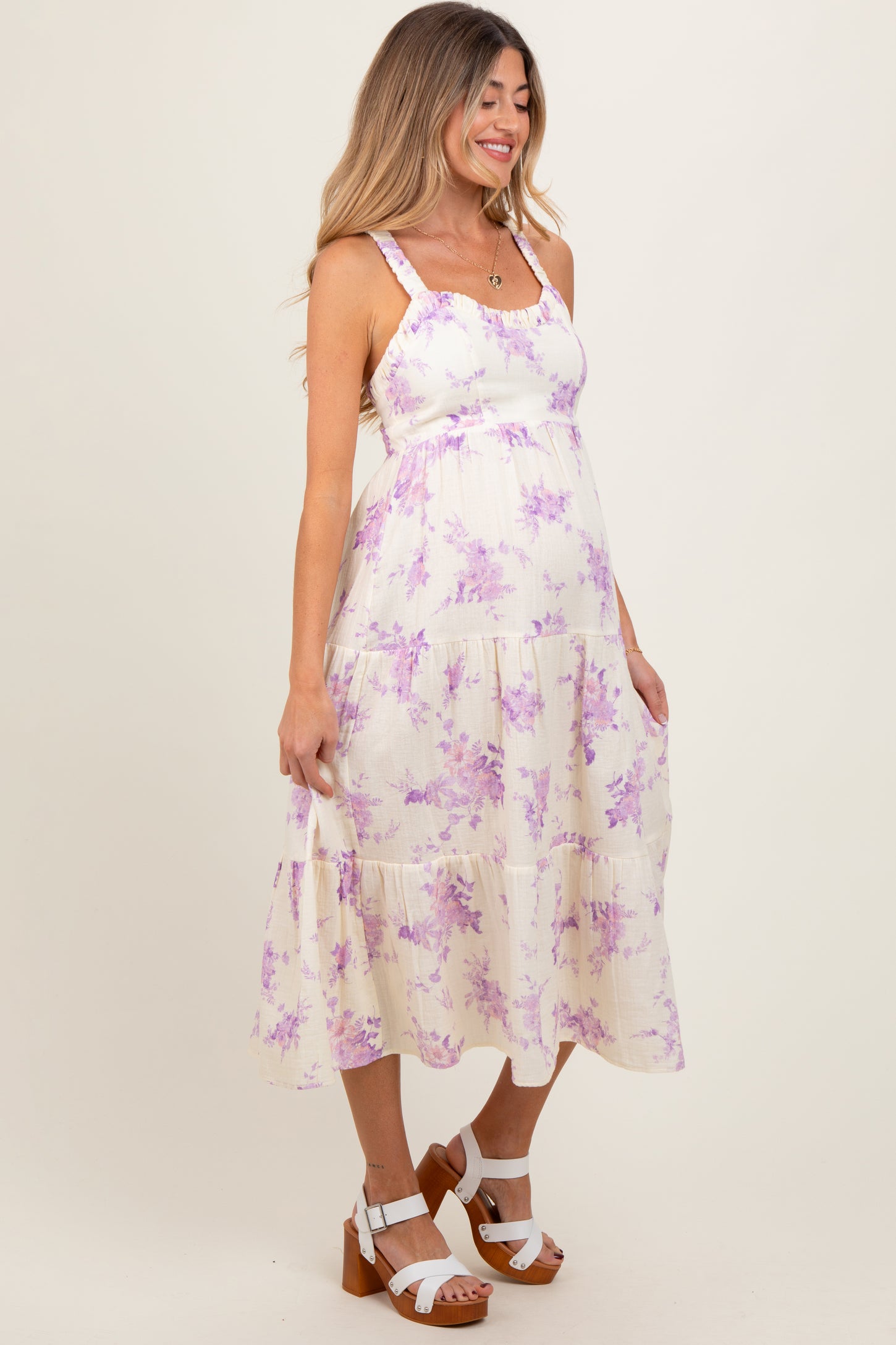woman wearing a cream maternity dress with lavender floral print and tiered skirt, showing her baby bump