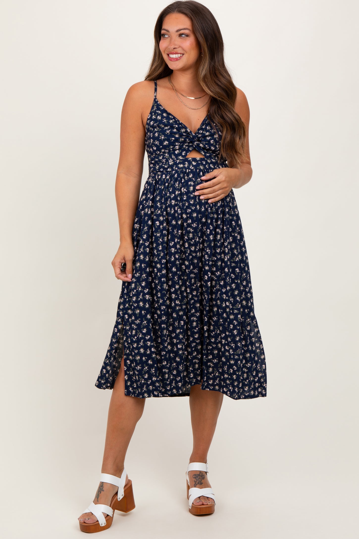 woman wearing a navy blue floral print maternity dress with a knot front and side slit, showcasing her baby bump