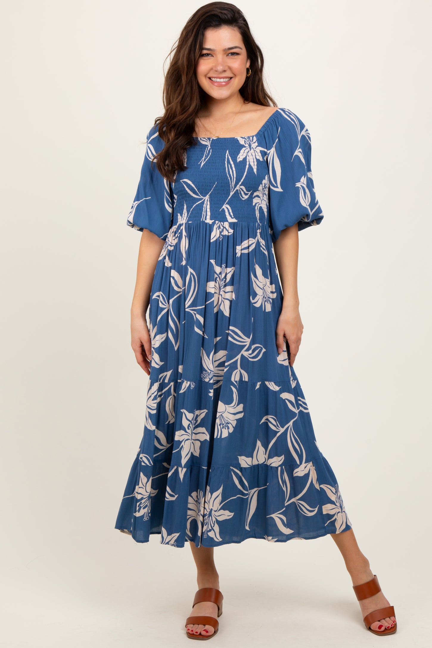 woman wearing a blue floral maxi dress with puff sleeves and a smocked bodice, standing on a neutral background