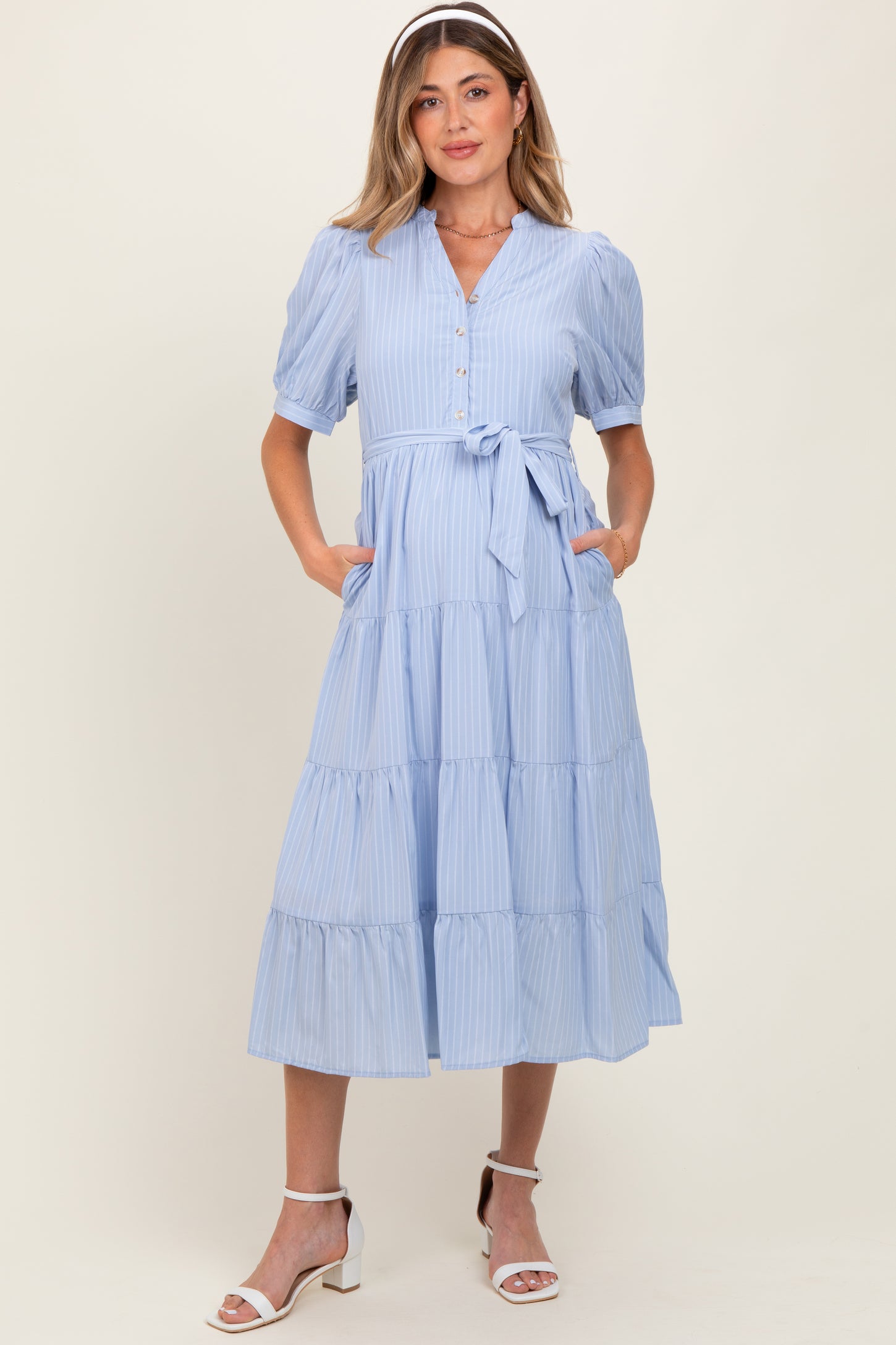 woman wearing a light blue striped maternity dress with short sleeves, button details, pockets, and a tie waist