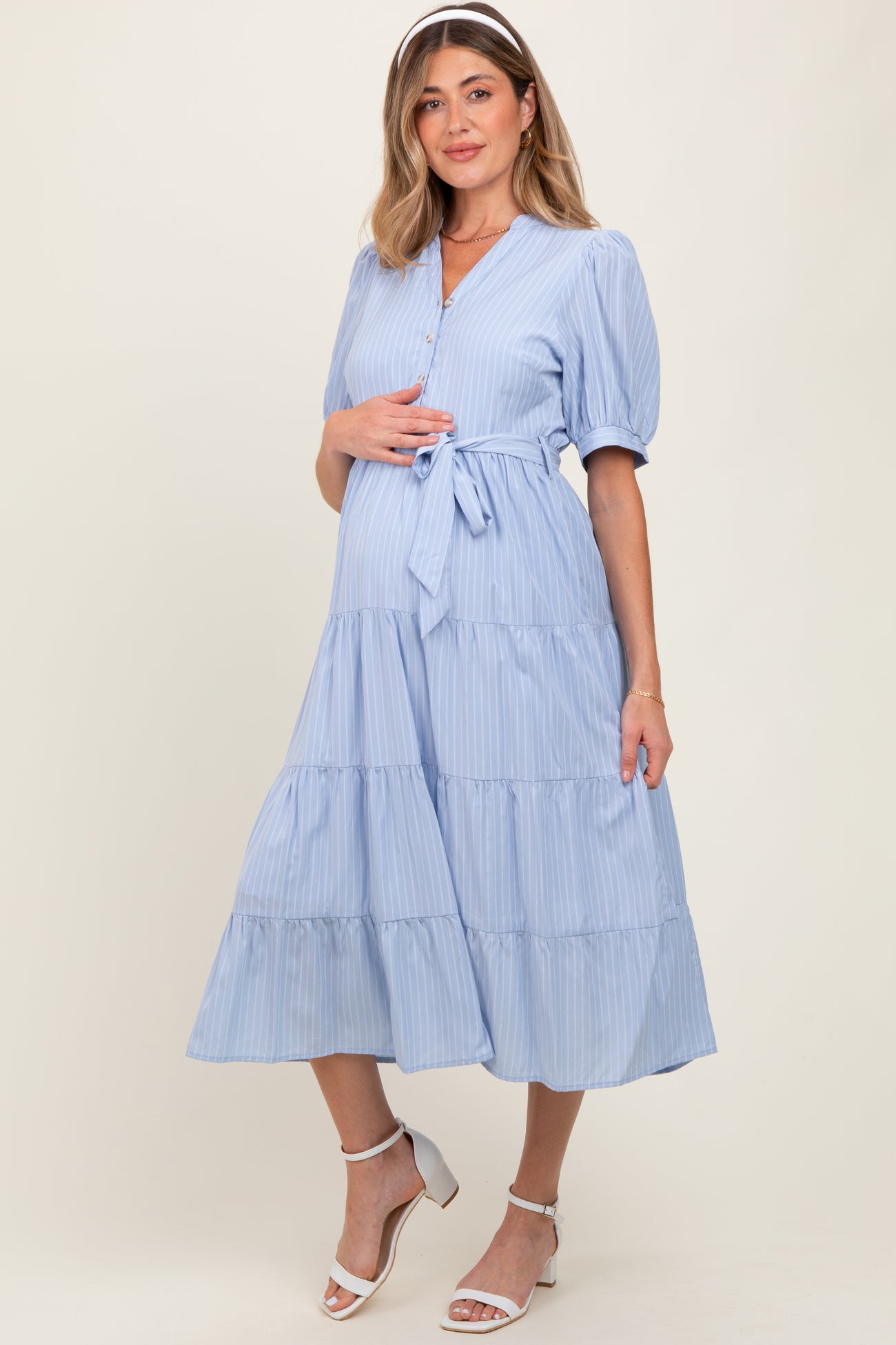 woman wearing a light blue maternity dress with tiered ruffles and a tie waist, holding her baby bump