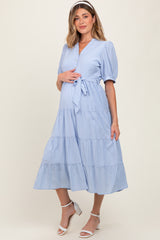 woman wearing a light blue maternity dress with tiered ruffles and a tie waist, holding her baby bump