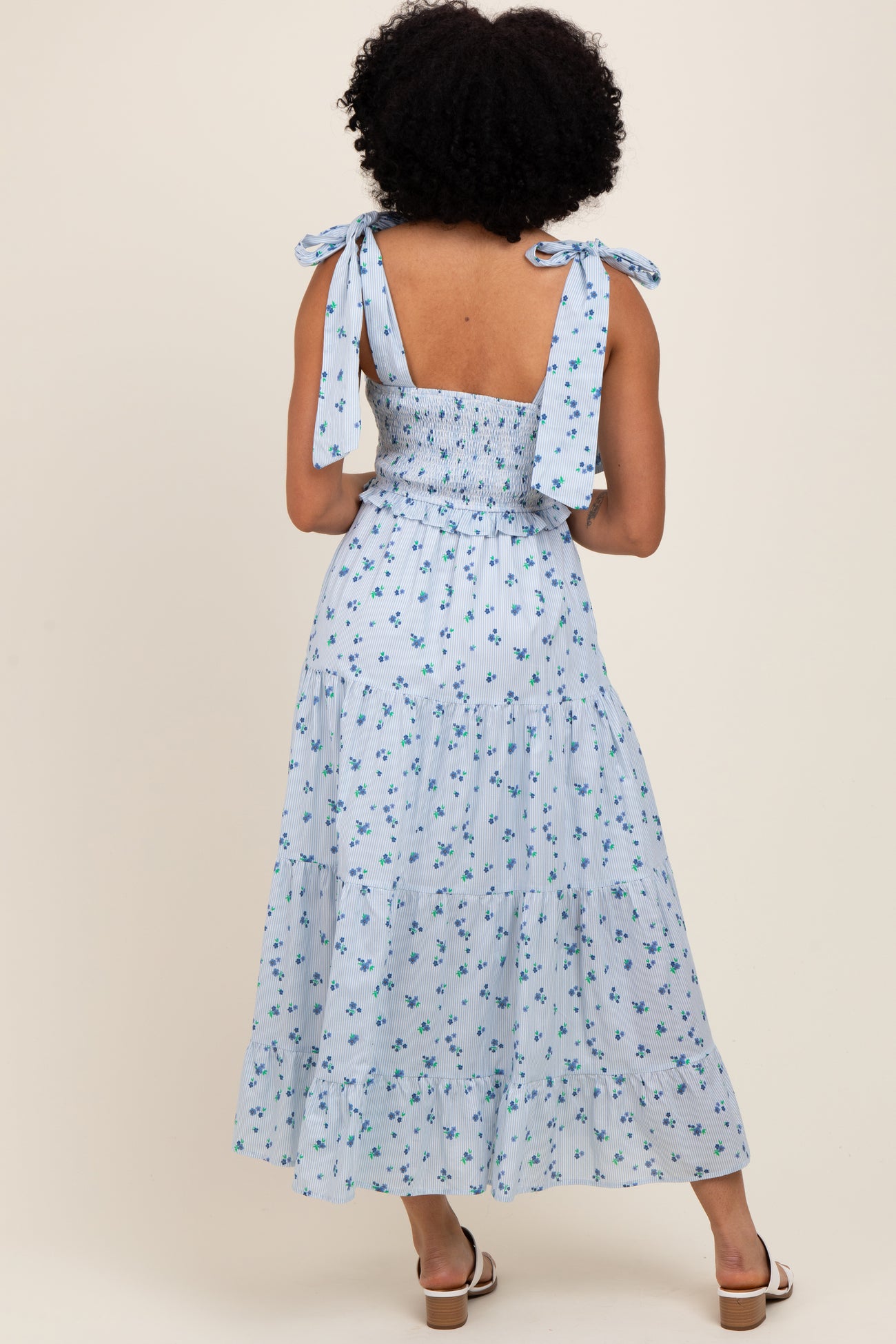 woman wearing a light blue floral print maxi dress with tie straps and a smocked bodice, shown from the back