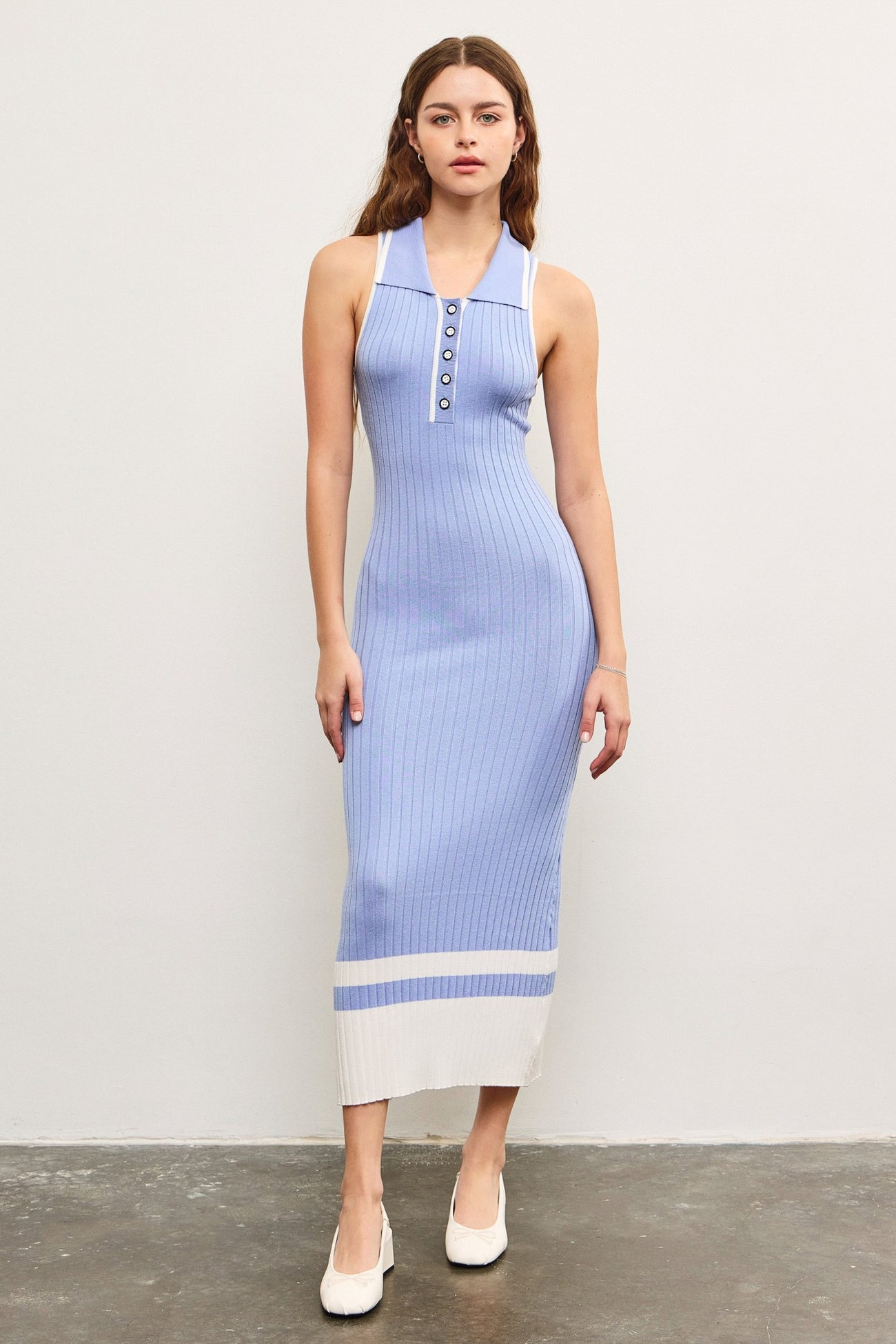 woman wearing a light blue ribbed midi dress with buttons and white accents, standing on a textured floor