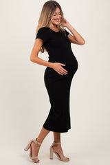 woman wearing a black fitted maternity dress and cradling her baby bump, standing in a side profile pose